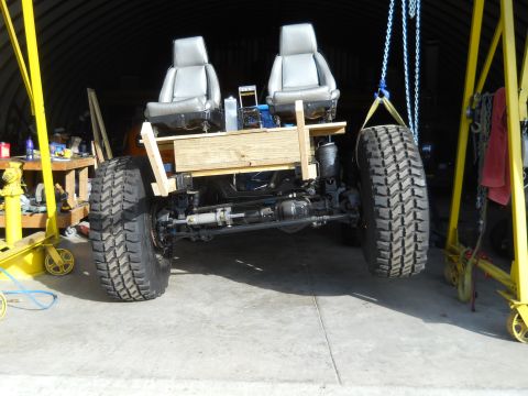 1992 Ford Bronco - A custom-built vehicle chassis with seats is being worked on, suspended by cranes in a garage.