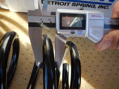 2003 Ford Crown Victoria - digital caliper measures a black coil spring on a tan pad beneath a box labeled Detroit Spring Inc.