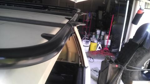 1985 Toyota 4Runner - Close-up view of a black roof rack and a curved protective bar mounted on a white vehicle.