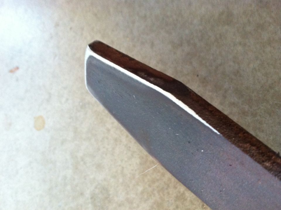 Close-up of a dark-colored vehicle part with a white edge, resting on a textured surface. Supermotors.net logo visible