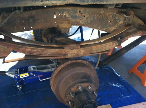1977 Ford F-350 - Close-up view of a vehicle's rear suspension system, including leaf springs and axle, with repair equipment present.