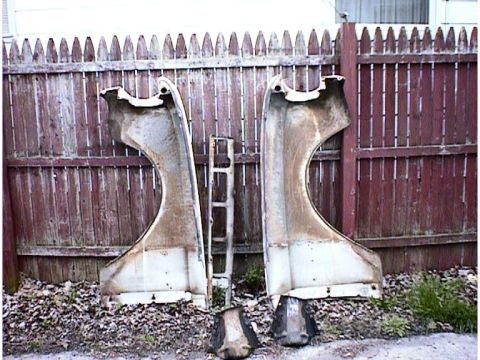 1960 Ford Falcon - Two weathered car fenders and a central trim piece are displayed outdoors against a rustic wooden fence.