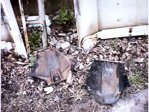 1960 Ford Falcon - Two unidentified, rusty metal car parts are visible on the ground, surrounded by debris and foliage.