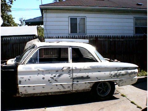1960 Ford Falcon - A white 1960 Ford Falcon sedan is seen from the side, with significant paint damage and some bodywork apparent.