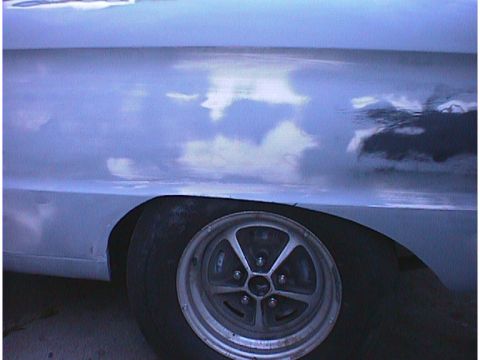 1960 Ford Falcon - The side of a car with a reflective surface shows clouds and a wheel with a five-spoke rim.