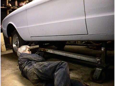1960 Ford Falcon - A person in overalls works on the underside of a 1960 Ford Falcon.