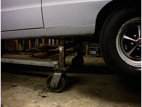 1960 Ford Falcon - A white car is elevated on jack stands, revealing its undercarriage and a glimpse of another vehicle in the background.