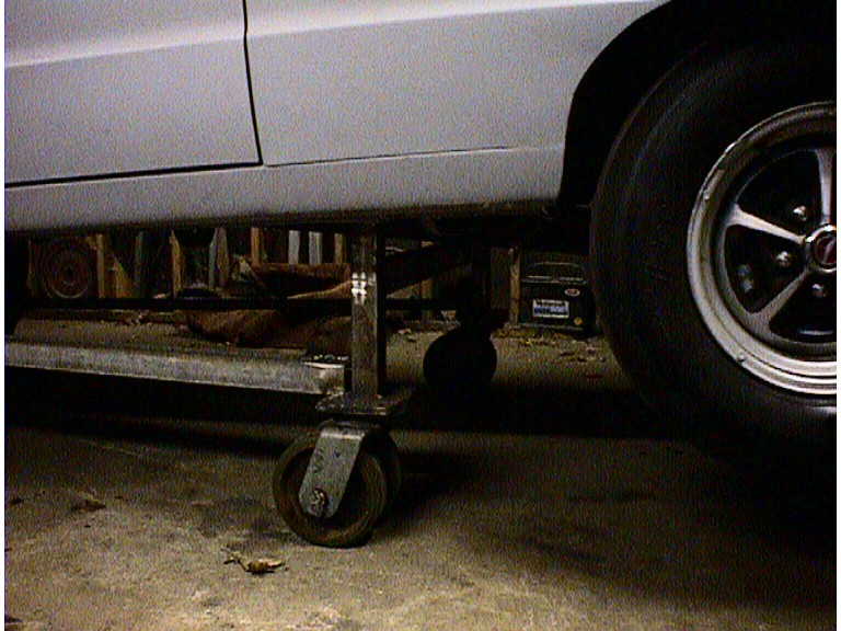 White car body on metal jack stands, close-up on side panel and wheel