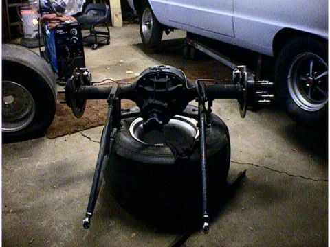 1960 Ford Falcon - A rear axle assembly is shown resting on a tire, with a portion of a white vehicle visible behind it.