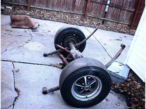 1960 Ford Falcon - A disassembled rear axle assembly with tires and shocks is shown resting on a concrete driveway.