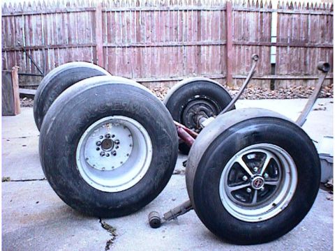 1960 Ford Falcon - Drag racing tires and suspension components are laid out on a concrete surface in front of a wooden fence.
