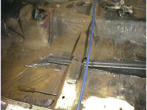 1960 Ford Falcon - The interior floor of a car shows significant rust and a screwdriver lying on the metal.