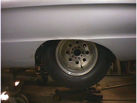 1960 Ford Falcon - A close-up view of a car's rear wheel well, showing a drag slick tire and a custom wheel, with the vehicle supported by jack stands.