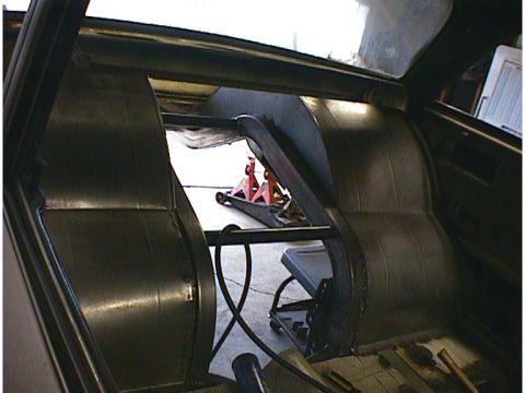 1960 Ford Falcon - The interior of a car is shown with a roll cage, modified rear seating area, and a floor jack visible through the rear window.