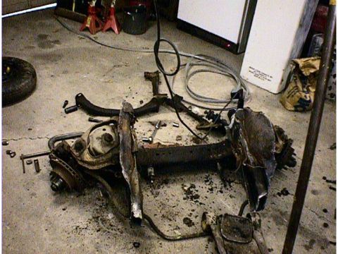 1960 Ford Falcon - A disassembled vehicle subframe lies on a garage floor, surrounded by tools and parts.