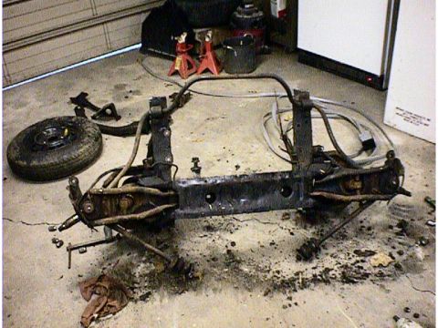 1960 Ford Falcon - A disassembled front subframe assembly, including suspension parts and a spare tire, lies on a garage floor.