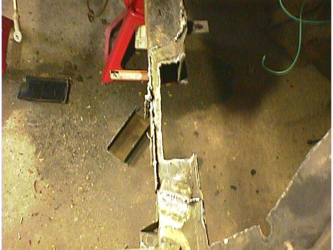 1960 Ford Falcon - A close-up view of a heavily rusted metal frame, supported by red jack stands, in a workshop setting.