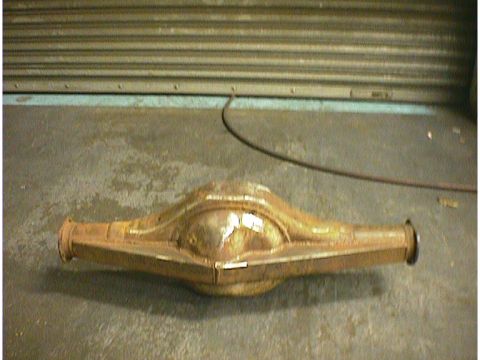 1960 Ford Falcon - A rusty rear axle housing sits on a concrete floor in front of a large, ribbed metal door.