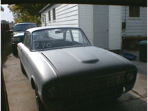 1960 Ford Falcon - A gray 1960 Ford Falcon is parked in a driveway next to a dark SUV, with a building in the background.