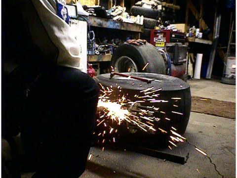 1960 Ford Falcon - Workshop scene with a person welding a large tire, sparks flying.