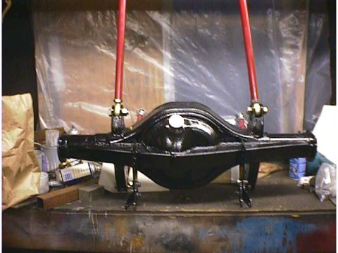 1960 Ford Falcon - A black rear axle assembly is shown suspended by red arms, resting on a workbench with various supplies in the background.