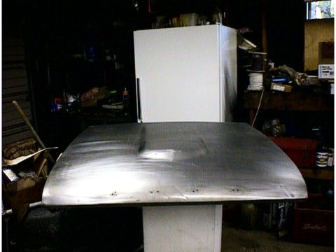 1960 Ford Falcon - A bare metal car hood is shown in a workshop setting, with a refrigerator and various tools in the background.