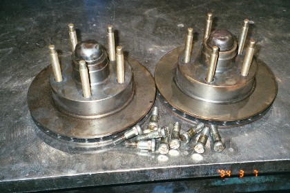 1960 Ford Falcon - Two brake rotors with wheel studs are shown next to a pile of loose wheel studs on a metal workbench.