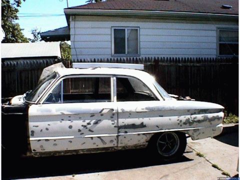 1960 Ford Falcon - A white 1960 Ford Falcon sedan shows significant paint damage and appears to be in a state of disrepair.