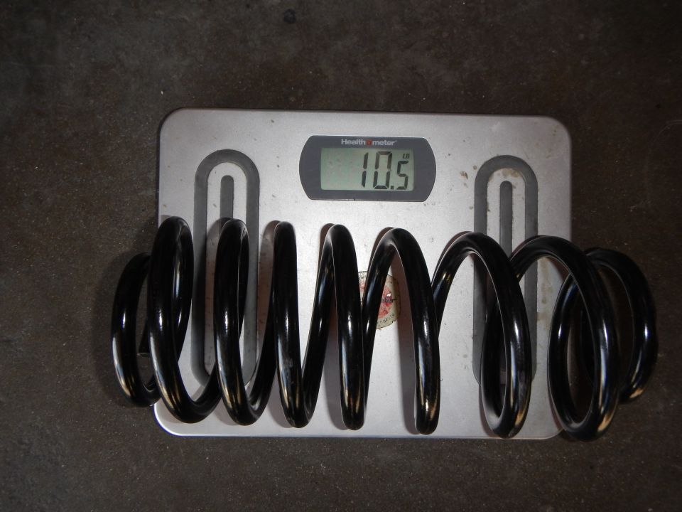 Black coil spring resting on a bathroom scale reading 10.5