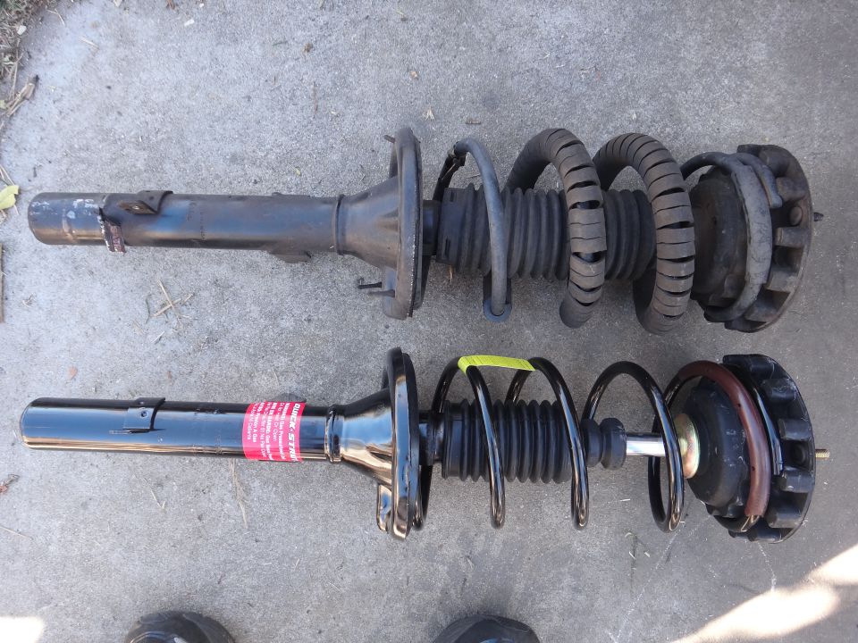 Two car struts with springs, one old and worn, the other new with a red label