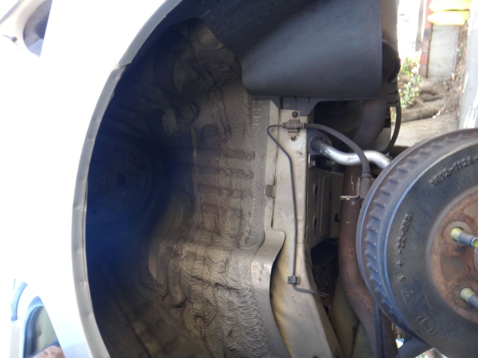 Close-up of a car's rear wheel well and suspension parts, showing brake rotor and undercarriage