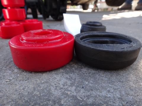 2003 Ford Taurus - New red polyurethane and old black rubber suspension bushings laid out on concrete.