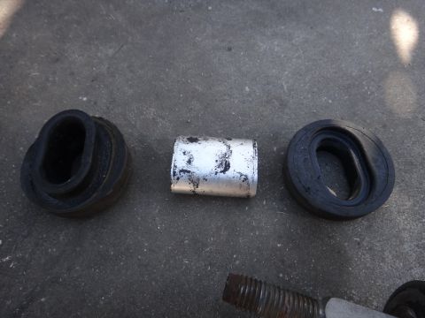 2003 Ford Taurus - Two rubber bushings and a metal spacer are laid out on a gray concrete surface.