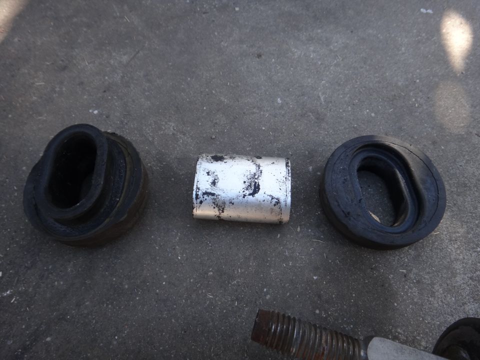 Three automotive suspension parts: two black rubber bushings and a silver metal spacer, on a concrete surface