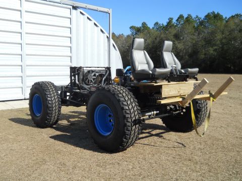 1992 Ford Bronco - A custom-built vehicle chassis with large tires and two seats is parked outdoors in front of a metal building.