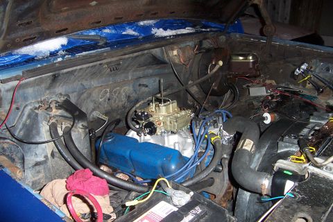 1980 Ford Bronco - The engine bay shows a carburetor and blue valve covers, with snow on the hood lining.