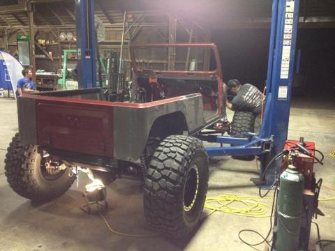 1985 Jeep CJ7 - A Jeep CJ7 body is elevated on a lift in a workshop, with a person working on the side.