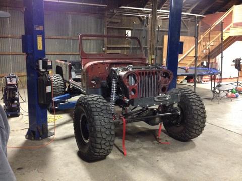 1985 Jeep CJ7 - This Jeep CJ-style vehicle is undergoing work on a lift, showing its front end and large off-road tires.