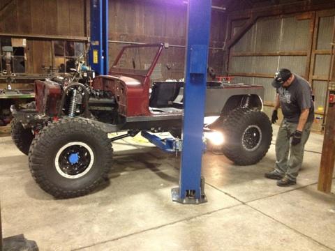 1985 Jeep CJ7 - A man inspects a Jeep CJ-series chassis being worked on in a garage.