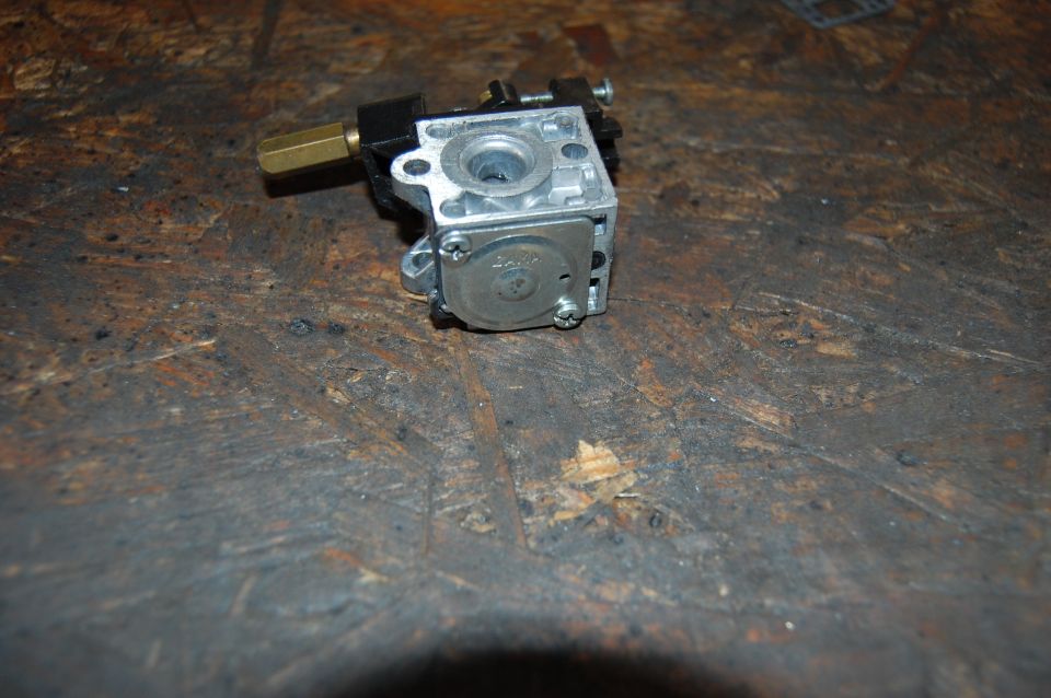 Close-up of a carburetor with a brass fitting on a wooden surface