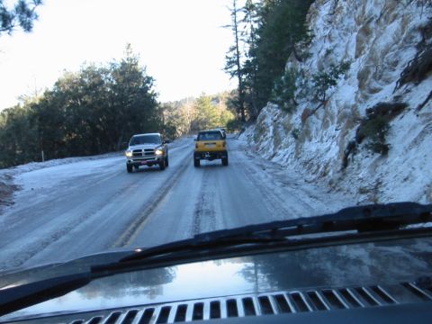 1985 Ford Bronco - Driving on a slippery, snow-dusted mountain road with two other trucks ahead.