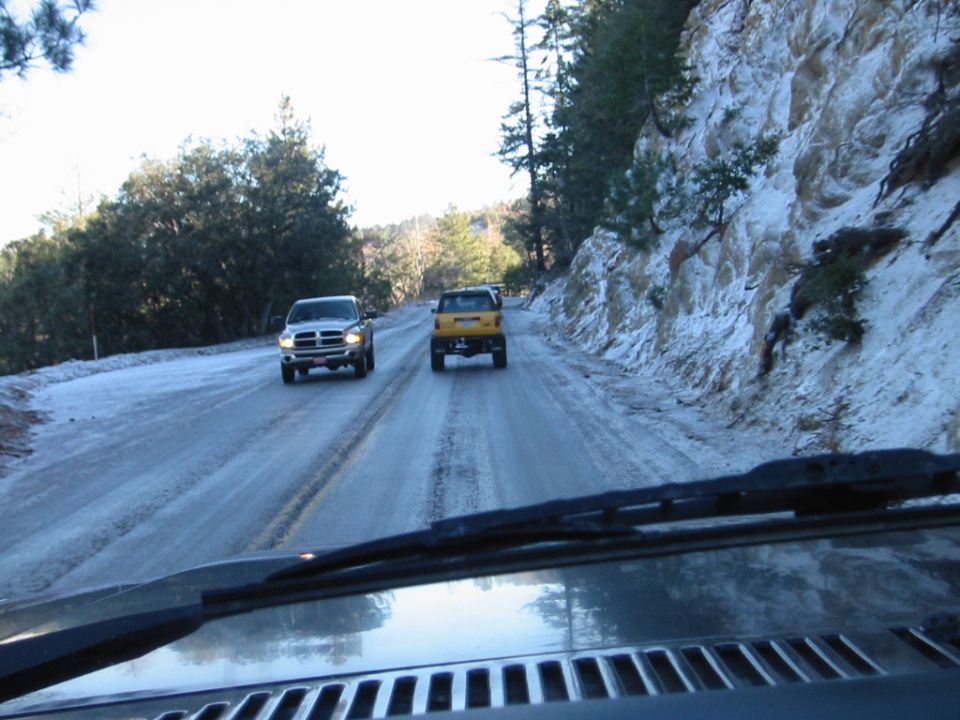 POV from dashboard on snowy mountain road with oncoming silver pickup and yellow SUV