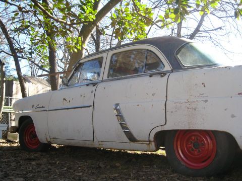 1952 Ford Customline - A weathered 1952 Ford Customline sedan sits outdoors under trees, its white paint showing significant rust.