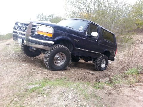 1995 Ford Bronco - 1995 Ford Bronco navigates a challenging off-road trail with its front wheels climbing an incline.