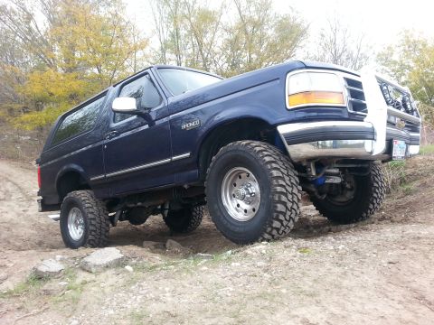 1995 Ford Bronco - A blue 1995 Ford Bronco navigates a rocky off-road path with its suspension articulated.
