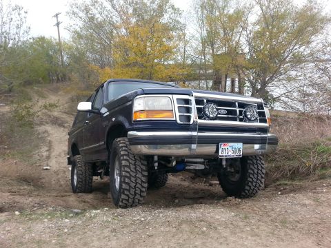1995 Ford Bronco - This lifted 1995 Ford Bronco is shown off-road, large tires and auxiliary lights on the grille.