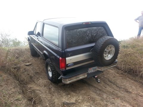 1995 Ford Bronco - Ford Bronco navigates an off-road trail, showing its rear profile and spare tire.