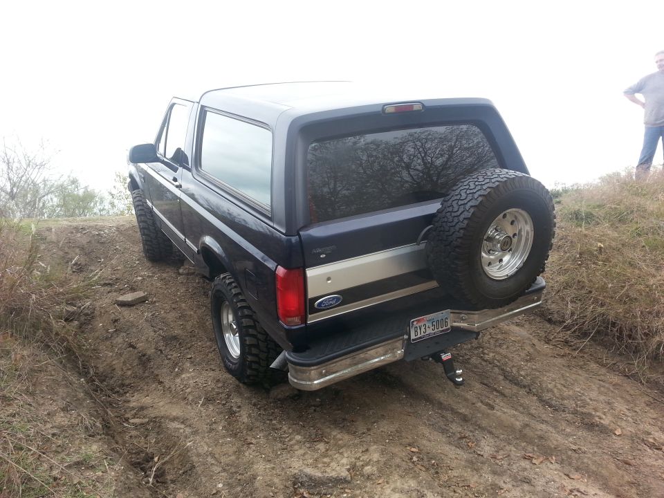 1995 Ford Bronco driving up a dirt hill with a spare tire mounted on the back