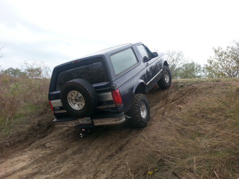 1995 Ford Bronco - Dark blue SUV navigates an off-road incline with a spare tire on the rear.