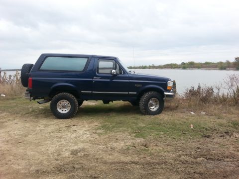 1995 Ford Bronco - Side view of a blue 1995 Ford Bronco parked near a lake under a cloudy sky.